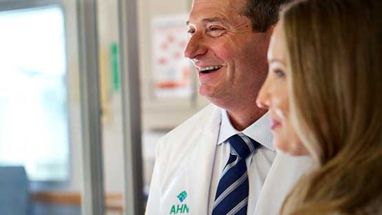 A doctor in a lab coat smiles while talking with a patient