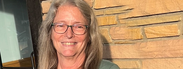 A woman in glasses smiling in front of a wall