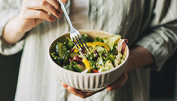 A person holding a bowl of salad holding a fork 