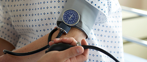 A patient in a gown having their blood pressure checked with a blood pressure cuff