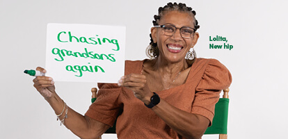 A woman named Lolita, who received a new hip, holding up a hand written sign that says Chasing grandsons again