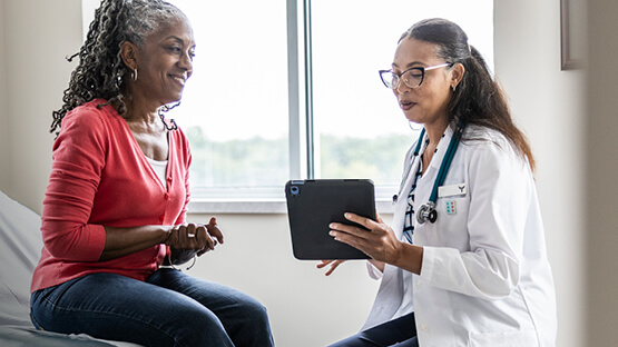 A doctor showing her tablet to her smiling patient as she sits on an exam table