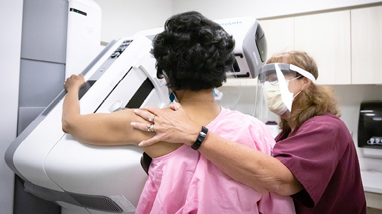 AHN nurse wearing PPE assisting a female patient to the correct position during her mammogram 