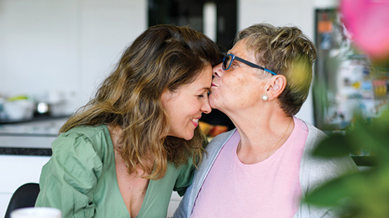Older mother kissing her smiling, middle-aged daughter on the forehead.