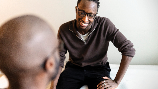 A smiling medical professional in a brown top looks kindly at a patient.