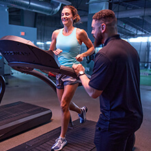 A physical therapist monitors his patient as she runs on a treadmill in a sports performance facility
