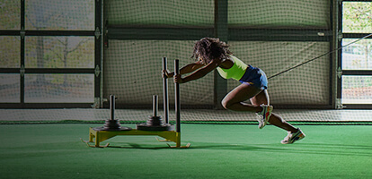 Athlete pushing a weighted sled while she runs on turf inside a training facility