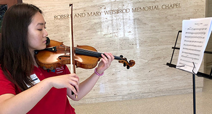 AHN volunteer in her red volunteer shirt playing her violin.