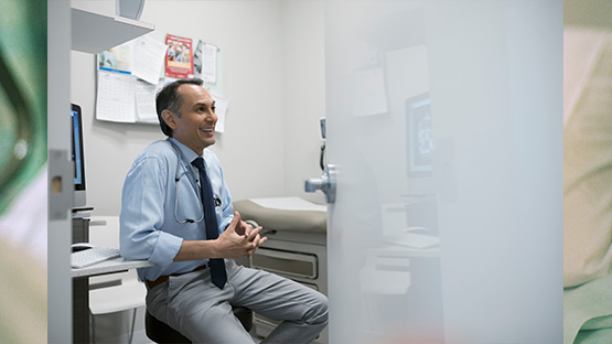 A doctor sitting in an examining room having a good time talking to a patient that is off camera.