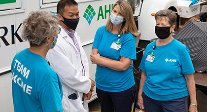 AHN volunteers in blue shirts and wearing masks talking to a doctor outside at a vaccine clinic.