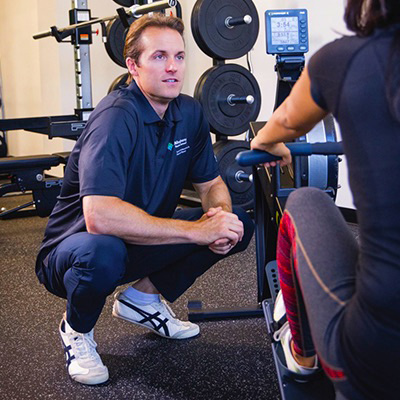 Trainer squatting down and talking to patient while she is doing her exercise.