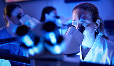 Two researchers look into microscopes in a lab.
