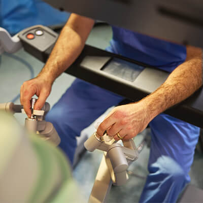 A surgeon in blue scrubs and mask operates a robotic surgical system.