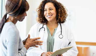 doctor smiling and listening as a female patient discusses her diagnosis