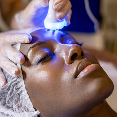 Patient receiving blue light therapy during a cosmetic dermatology procedure to improve skin texture and reduce acne.