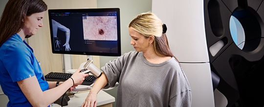 Medical professional examining a patient's mole with a dermatoscope and digital mole analysis software
