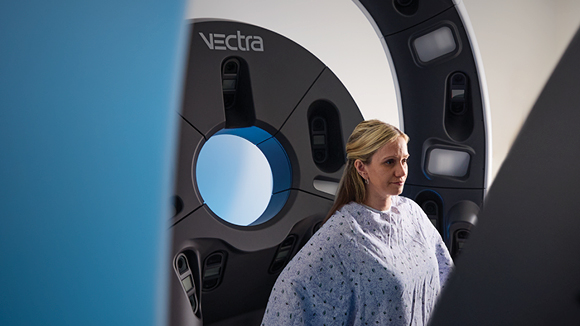 Woman in gown seated inside Vectra WB360 scan machine for early skin cancer detection.