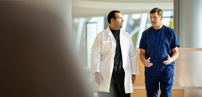 A medical professional in a white coat looks at a patient's chart while talking.