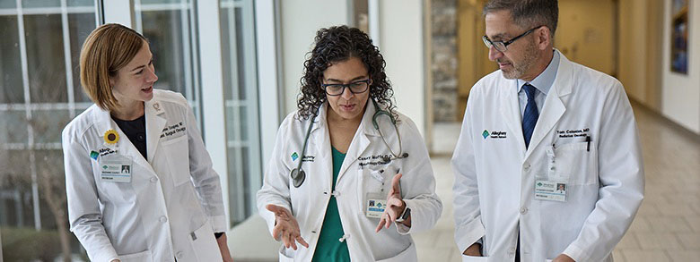 Dr. Coopey chatting with two other AHN cancer institute specialist while walking down a hallway.