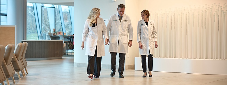 Three doctors in lab coats talking to each other while walking through a hallway 