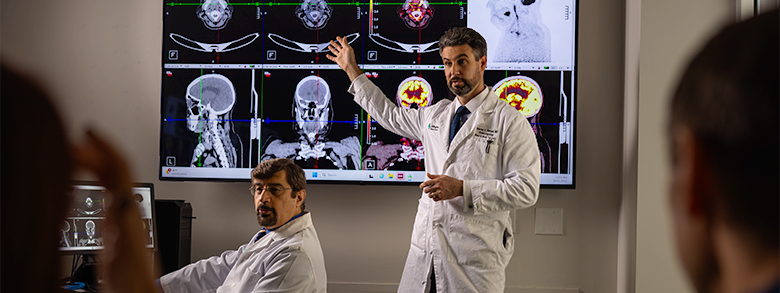 Medical professionals in white coats look at brain scans on a large screen in a meeting room.