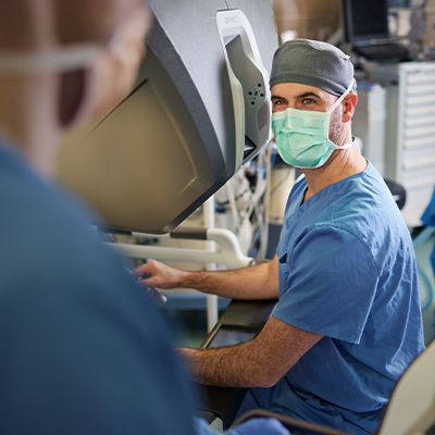 A white medical professional in blue scrubs and a mask operates equipment.