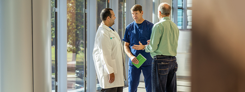 Three men, including two medical professionals, talk in a brightly lit hallway.