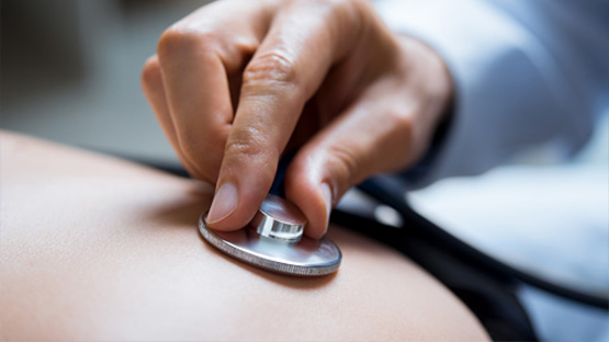 Close up view of a doctor's hand checking a patients heartbeat with a stethoscope