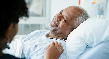 A patient in a hospital bed smiling as a hand is placed on his shoulder