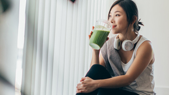 A woman smiling as she sips a fresh green smoothie.