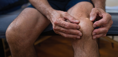 An elderly man sitting on a couch and holding his knee.