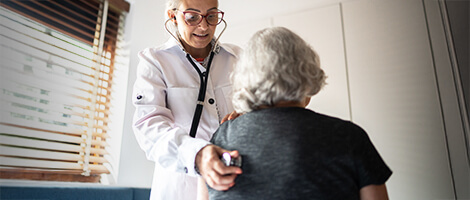 A doctor listens to an older woman's breathing with a stethoscope