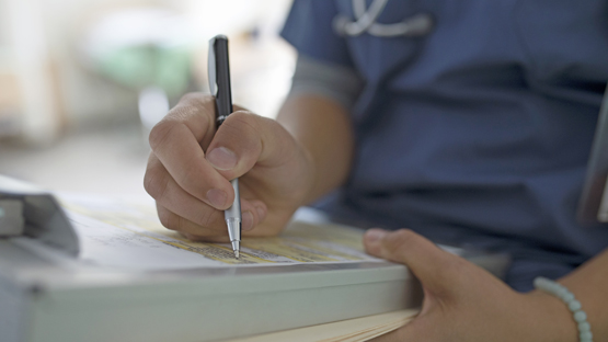 image of a chronic care doctor writing on a medical chart after treating patient for their chronic heart failure.