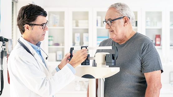 A doctor weighing a patient who is standing on a scale.