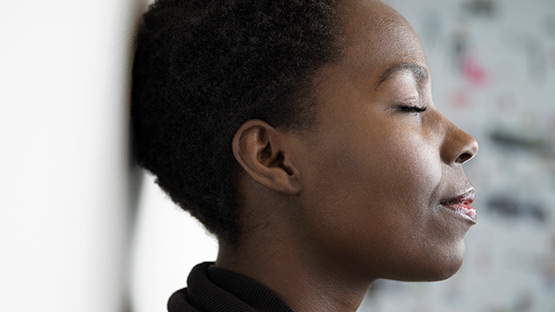 A woman leaning her head against the wall while having her eyes closed.