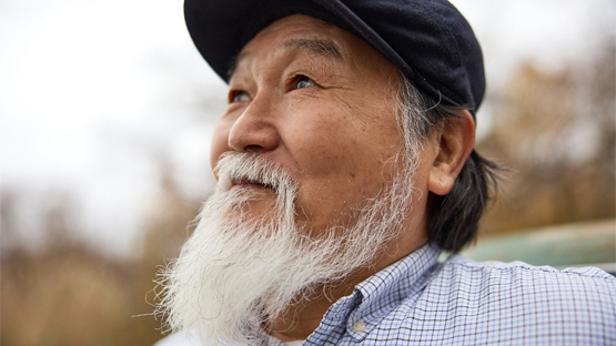 An Asian man with a white beard and a hat looking up into the sky and thinking about scheduling an AHN appointment.
