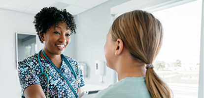 Smiling nurse holding a tablet talking to a female patient in exam room