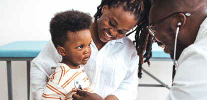 Smiling mother holds her toddler son as a doctor listens to the child's heartbeat with a stethoscope