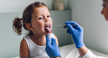 A doctor in gloves swabbing a young girl's tongue in an exam room 