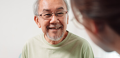 A patient with gray hair and glasses smiles while consulting with a doctor.