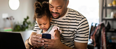 Man sitting with young child both looking at his phone