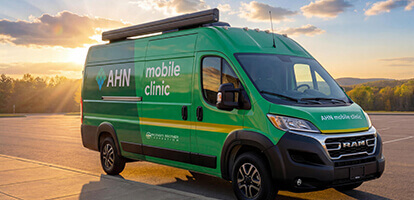 The green AHN Primary Care Mobile Clinic is parked on a scenic road with sunset in the background.