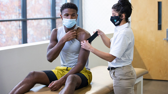 AHN therapist applies kinesiology tape to a student athlete's shoulder