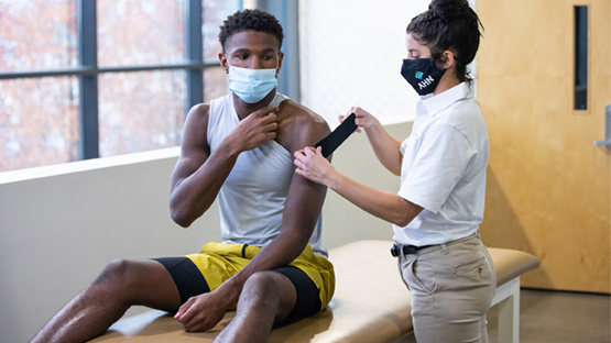 AHN therapist applies kinesiology tape to a student athlete's shoulder.