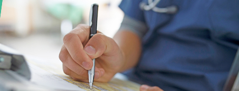 A doctor writing on a chart while sitting down at a desk.