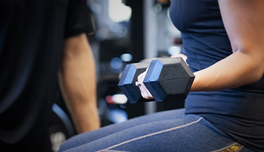 A person curls a black dumbbell with focus in a gym.