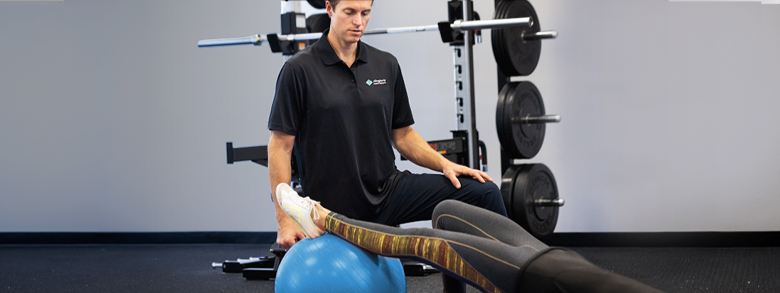 A medical professional helps a person stretch with a blue exercise ball.