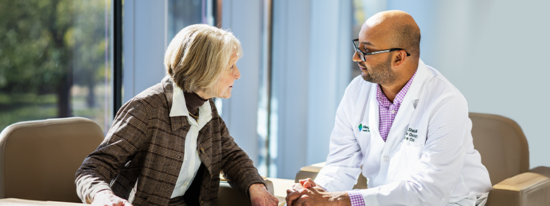 A white woman and a South Asian medical professional in a white coat talk to each other.