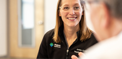 A smiling medical professional in a black jacket looks at a patient.