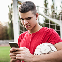 A young man holding a ball under his arm while scheduling an appointment on his phone.